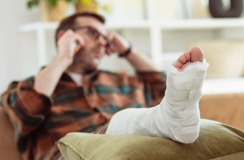 Man propping his foot up on a pillow and calling a top-rated personal injury lawyer after a serious accident.