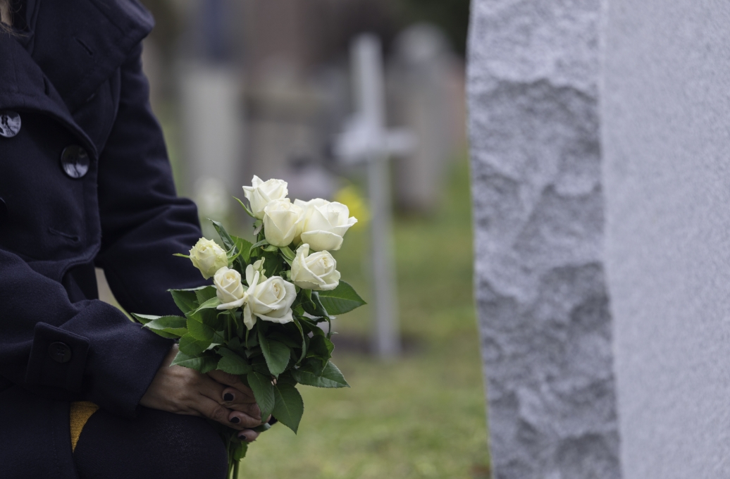 Loved one holding white flowers by a grave after experiencing a wrongful death case.