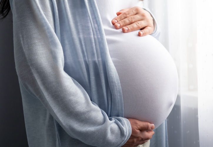 mother holding her pregnant belly while facing a window