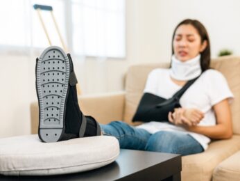 woman with neck brace, arm sling and foot in a cast sitting on the couch