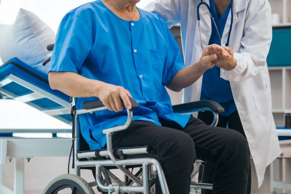 Man sitting in a wheelchair and holding a doctor's hand.