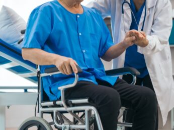 Man sitting in a wheelchair and holding a doctor's hand.