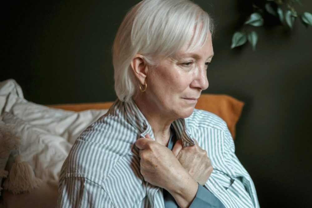Older woman sitting on a couch looking sad.