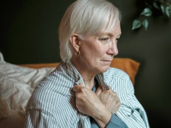 Older woman sitting on a couch looking sad.