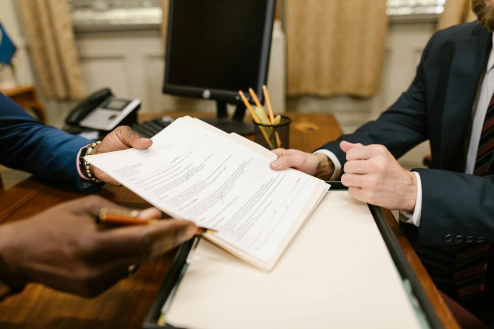 Two sets of hands holding a piece of paper across a desk.
