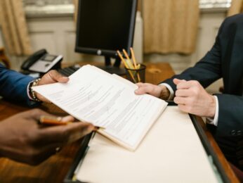 Two sets of hands holding a piece of paper across a desk.