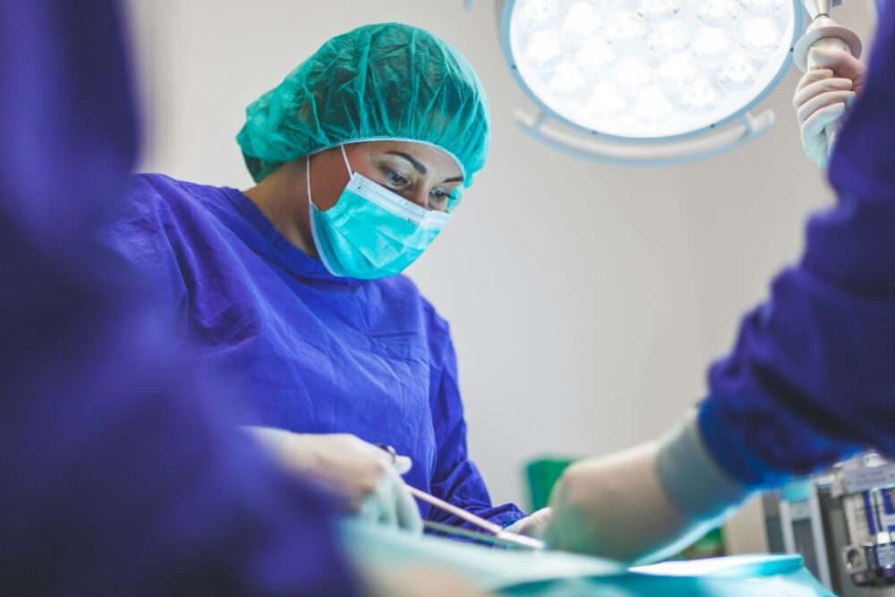 Doctor in scrubs and a mask doing stitches on a patient.