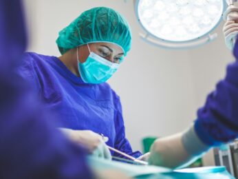 Doctor in scrubs and a mask doing stitches on a patient.